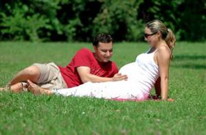 Беременная женщина и мужчина сидят на траве
